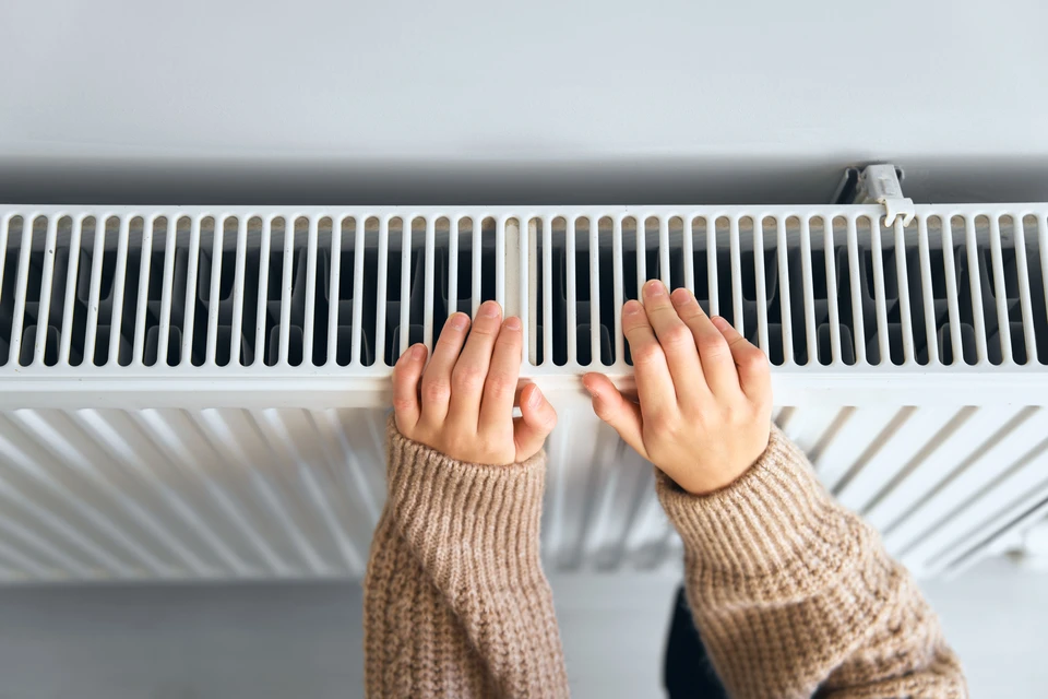 Intérieur résidentiel avec technicien en combinaison rouge et bleue installant un radiateur blanc à ailettes sur mur gris
